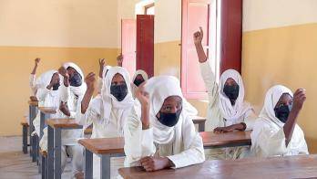 Teenage girls in Sudan raise their hands in class. 