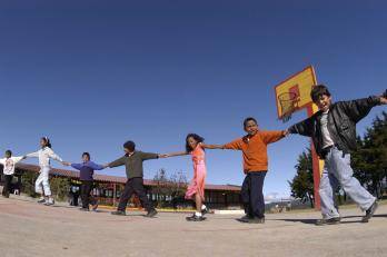 Children in Honduras hold hands and gather in a line while playing on the basketball court.